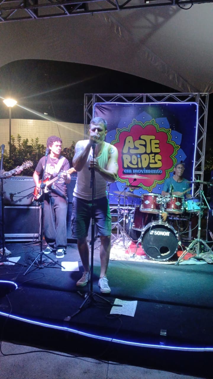 Vocalista em primeiro plano com guitarrista e baterista ao fundo