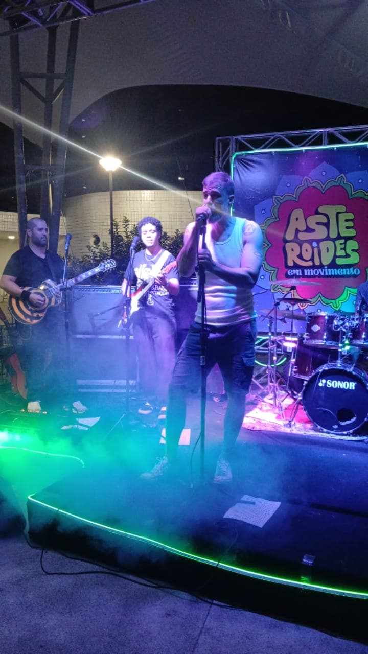 Vocalista cantando em primeiro plano com os guitarristas ao fundo